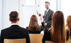 A professional man in a suit presenting to a group of people during scrum master training