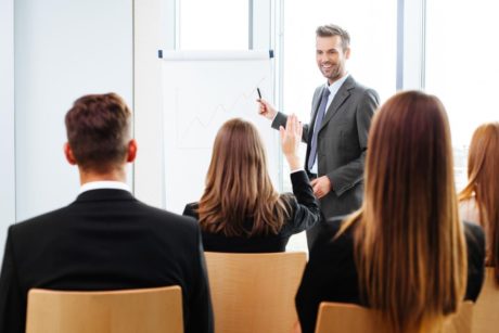 A professional man in a suit presenting to a group of people during scrum master training