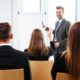 A professional man in a suit presenting to a group of people during scrum master training