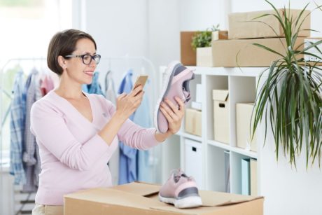 A woman holding shoes while checking her phone, possibly managing her Amazon FBA business