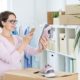 A woman holding shoes while checking her phone, possibly managing her Amazon FBA business