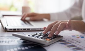 a person calculating on a desk with a laptop, illustrating lean accounting practices for efficient financial management