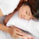 A woman sleeping peacefully in bed, with her hand resting on her wrist. Tips for better sleep.