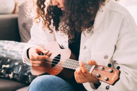 A woman skillfully demonstrates How to Play Ukulele on a cozy couch, showcasing her musical talent and passion