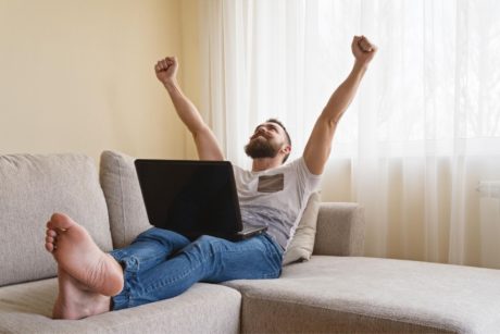 a man relaxes on a couch with his feet up, working on a laptop while exploring how to get jobs on upwork