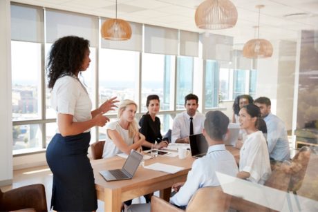 a woman in a business suit presents to a group during a sales presentation course