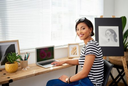 A woman sitting at a desk with a laptop, engaged in selling art online