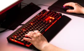 A person typing on a keyboard with a red light, developing a JavaScript Battle Game.