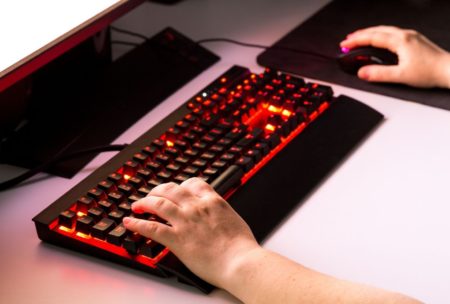 A person typing on a keyboard with a red light, developing a JavaScript Battle Game.