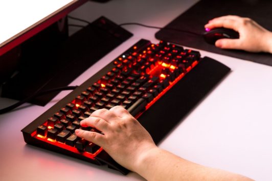 A person typing on a keyboard with a red light, developing a JavaScript Battle Game.