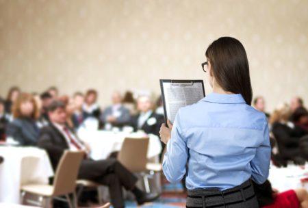 woman speaking in front of large audience