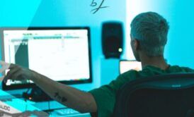 a man sits at a desk with a computer and microphone, engaged in an edm production course