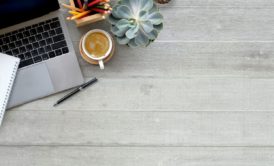 silver laptop paper plant cup of coffee on light wooden desk