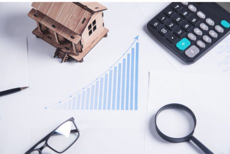 wooden house model calculator pair of glasses magnifying glass and bar graph in the middle