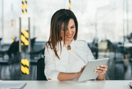 successful woman in white suit smiling and using ipad