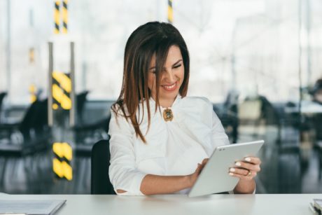 successful woman in white suit smiling and using ipad