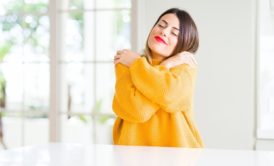 woman in yellow sweater giving herself a hug