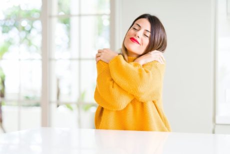 woman in yellow sweater giving herself a hug