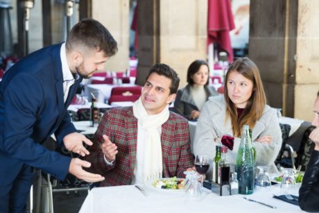 waiter in blue suit dealing with two angry customers