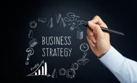 man writing the word business strategy and other buiness-related illustrations on a blackboard