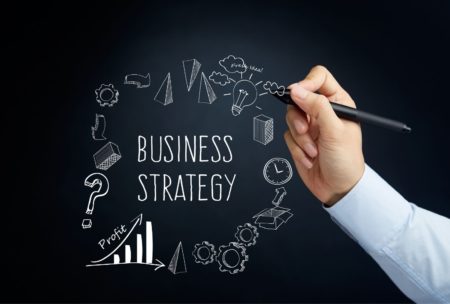 man writing the word business strategy and other buiness-related illustrations on a blackboard