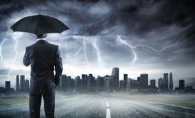 man wearing a suit and holding a black umbrella in the middle of a thunderstorm