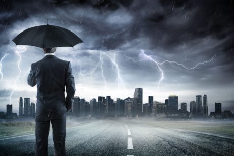 man wearing a suit and holding a black umbrella in the middle of a thunderstorm
