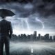 man wearing a suit and holding a black umbrella in the middle of a thunderstorm