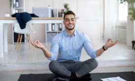 man in blue top meditating on black yoga mat