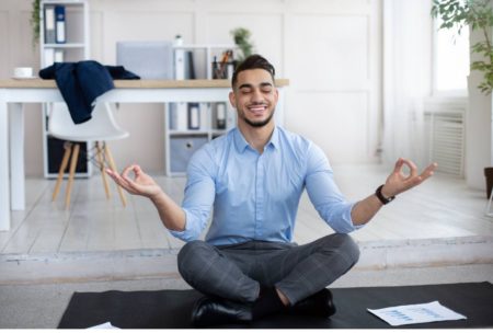 man in blue top meditating on black yoga mat