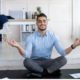 man in blue top meditating on black yoga mat