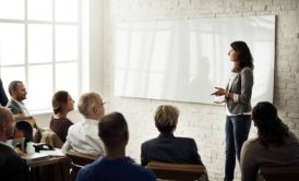 female lecturer in grey sweatshirt talking to a group of corporate people