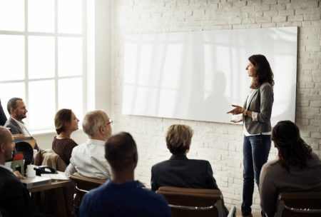 female lecturer in grey sweatshirt talking to a group of corporate people