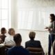 female lecturer in grey sweatshirt talking to a group of corporate people