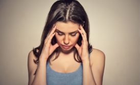 woman in grey top holding her head with both hands