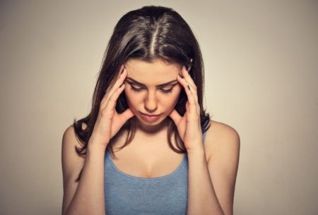 woman in grey top holding her head with both hands