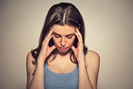 woman in grey top holding her head with both hands