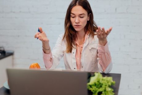 woman in white top talking to someone virtually through laptop