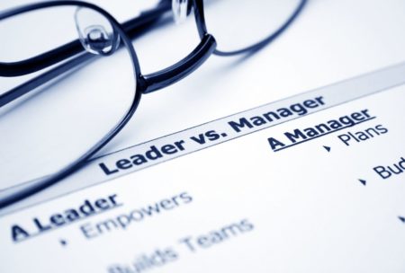 a piece of paper with the label leader versus manager in the background and a pair of glasses with black frame