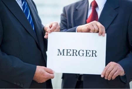 two men wearing suits holding white paper with the word merger