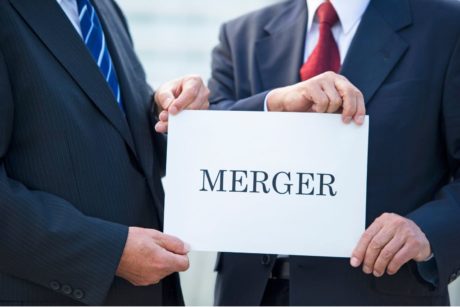 two men wearing suits holding white paper with the word merger