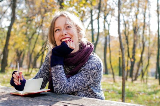 smiling woman wearing purple sweater and scarf outdoors journaling for self discovery