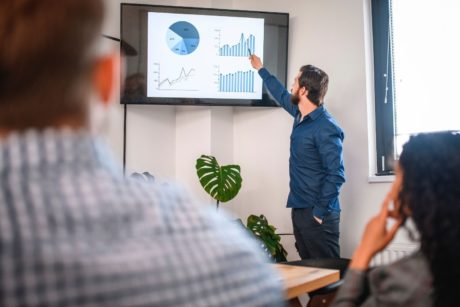 man in blue top presenting to a team in the boardroom