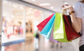 womans hand carrying multi colored shopping bags