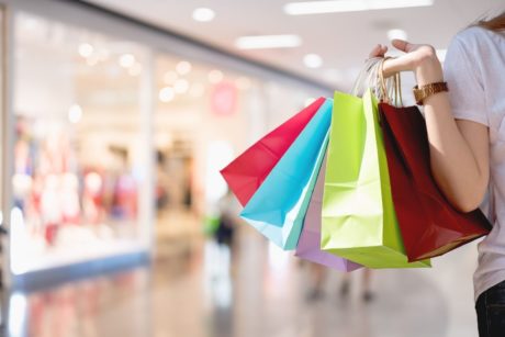 womans hand carrying multi colored shopping bags