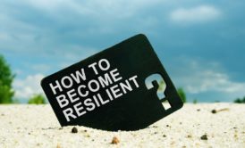 how to become resilient printed on black card lodged on white sand