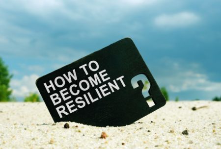 how to become resilient printed on black card lodged on white sand