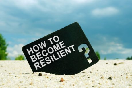 how to become resilient printed on black card lodged on white sand