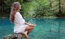 woman wearing white sitting on a rock meditating by a river