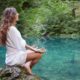 woman wearing white sitting on a rock meditating by a river